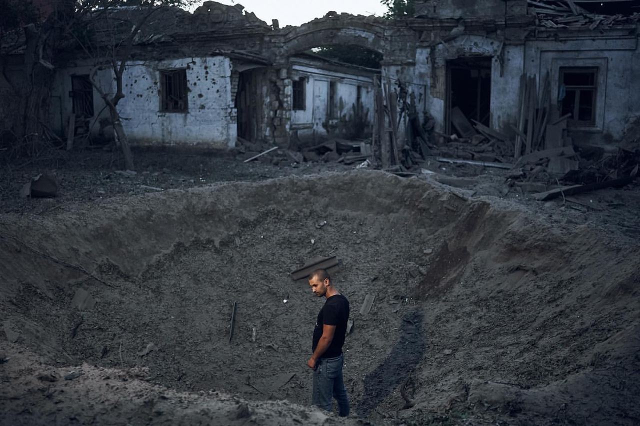 мужчина возле воронки и разбомбленных домов