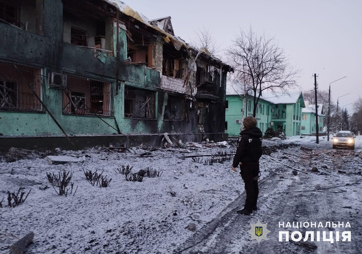 Поліцейський дивиться на обстріляну російськими загарбниками зелену будівлю на Донеччині