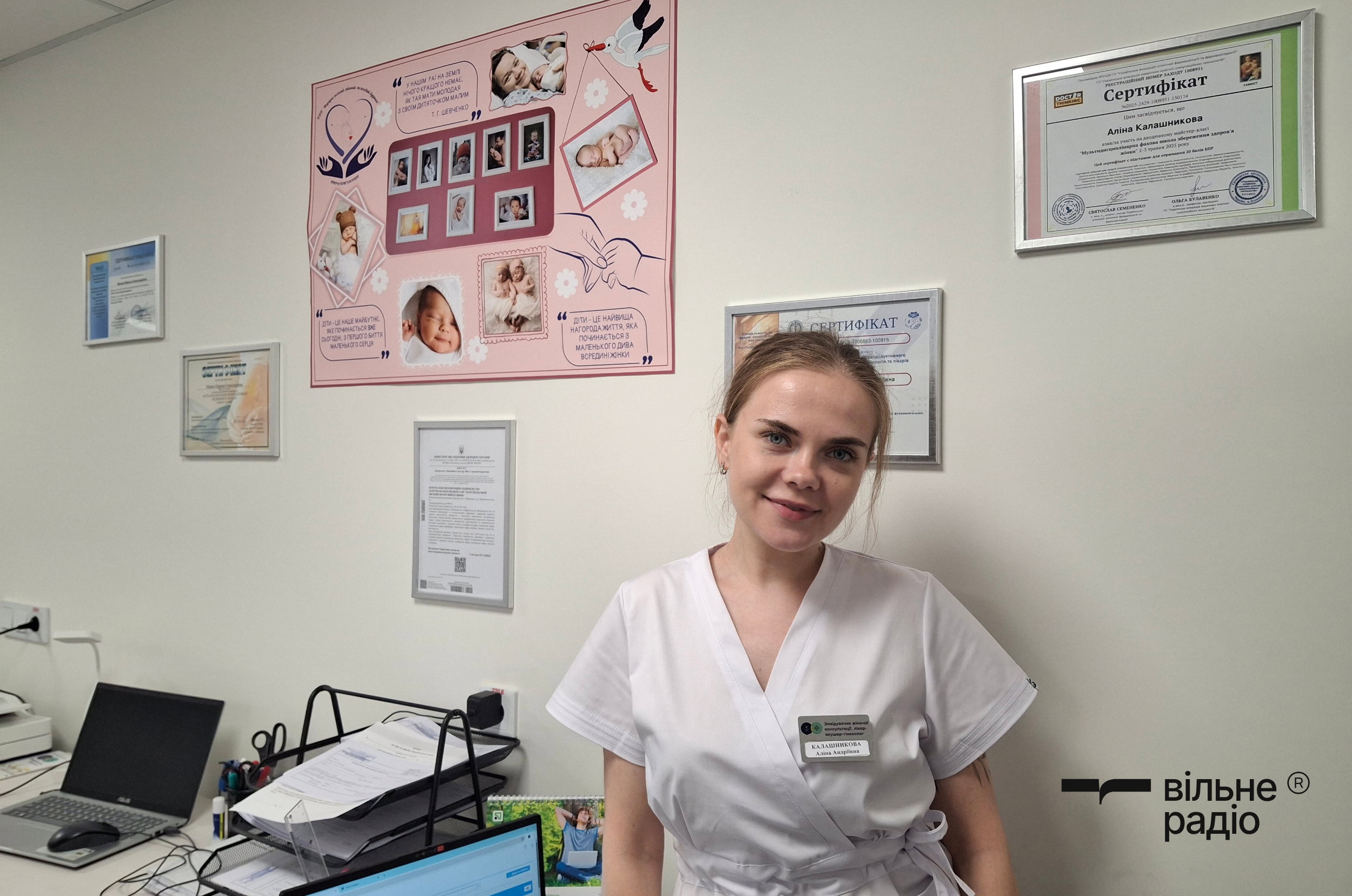 Заведующая женской консультацией Алина Калашникова напротив стенда с фотографией из мариупольского городского роддома