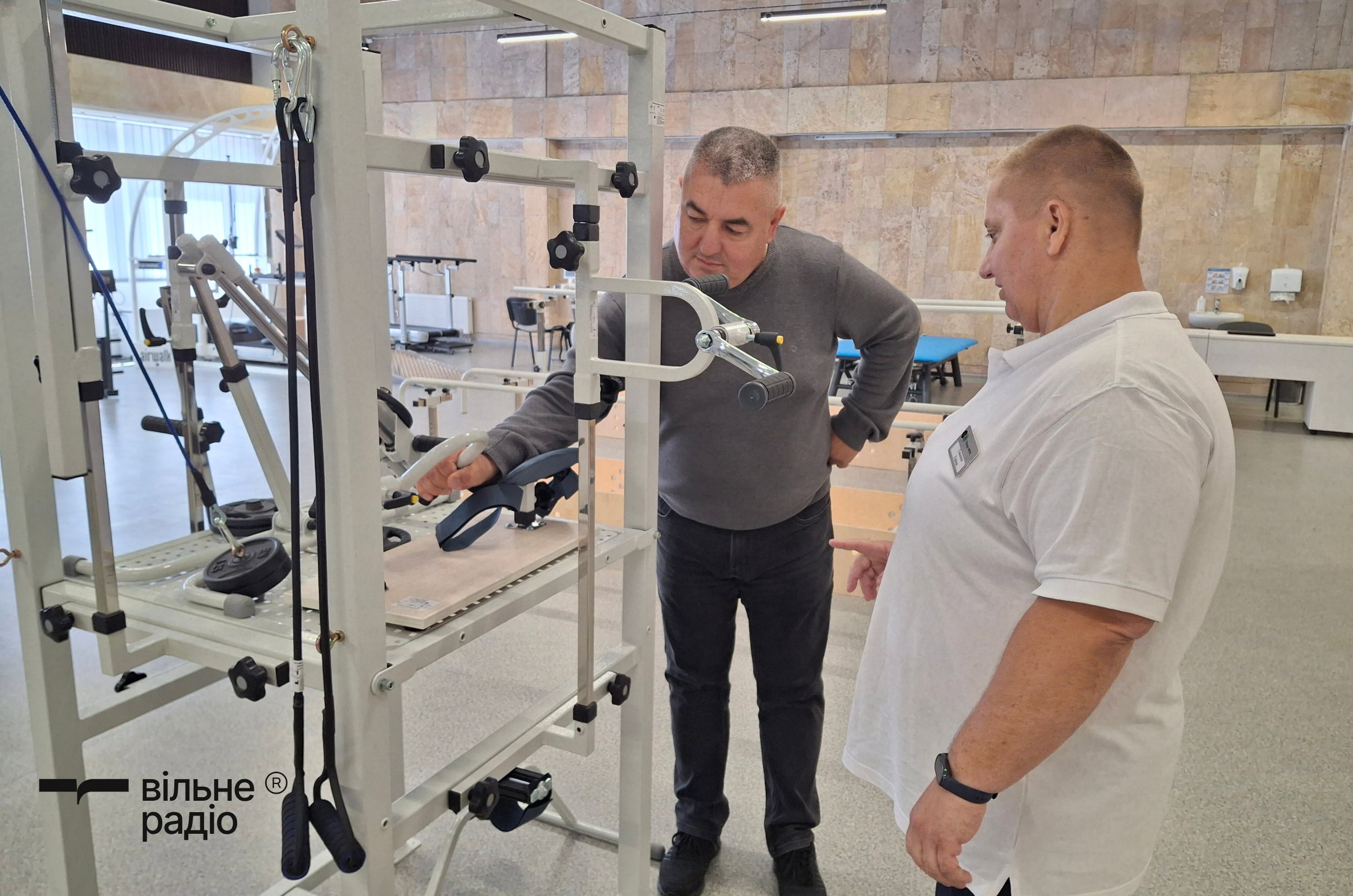 Врач физической реабилитационной медицины Анна Ганенко показывает ветерану Юрию Радникову, как пользоваться тренажером